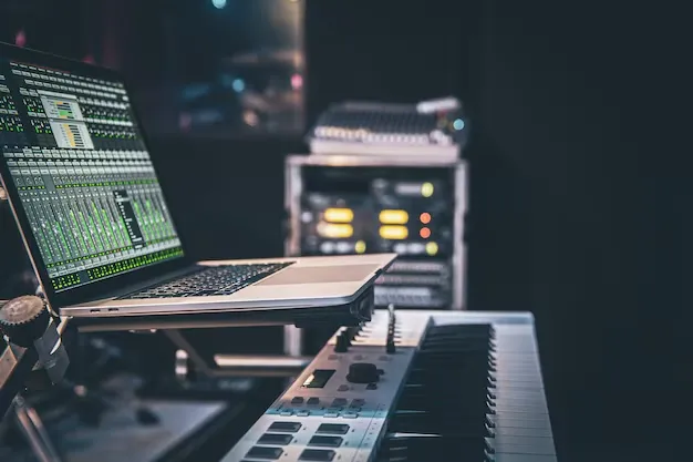 Laptop running music production software beside a keyboard